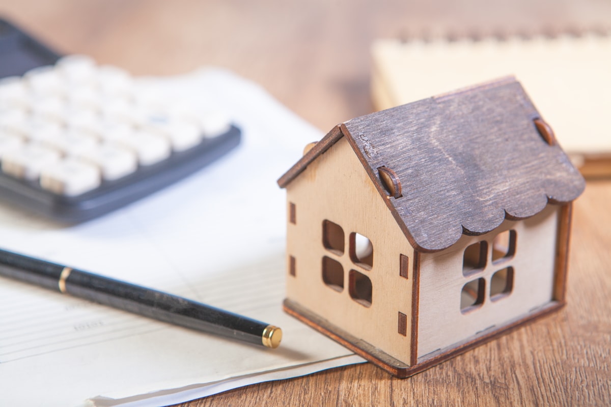 A wooden house model beside a calculator and notebook